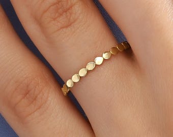 Könnte beinhalten: Ein goldener Ring mit einer Reihe kleiner, gleichmäßig verteilter kreisförmiger Akzente. Der Ring befindet sich an einem Finger, wobei die Hand und ein blauer Hintergrund sichtbar sind. Das Design des Rings ist schlicht und elegant. Durchmesser ca. 1,5 cm.