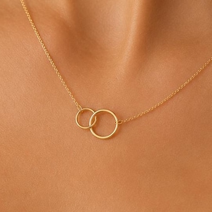 May include: A gold-toned necklace featuring two delicate, interlocking circular pendants suspended from a thin, matching chain. The design consists of one smaller circle linked to a slightly larger circle, creating a simple, continuous geometric shape.