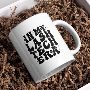 May include: White ceramic mug with the text "IN MY LASH TECH ERA" in black, retro-style lettering. The mug is inside a white box filled with brown crinkle paper. The mug has a white handle.