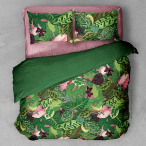 Könnte beinhalten: Ein grünes und rosa Bettwäsche-Set mit einem tropischen Blatt-Muster. Der Bettbezug ist einfarbig grün und die Kissenbezüge haben einen rosa Hintergrund mit grünen Blättern und Blumen.