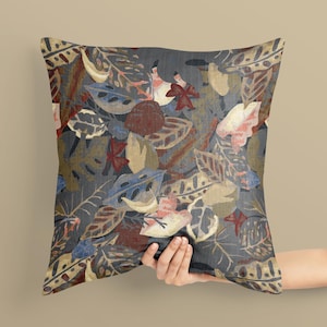Könnte beinhalten: Dekoratives Zierkissen mit einem botanischen Blattmuster. Das Kissen hat einen dunkelgrauen Hintergrund mit einem sich wiederholenden Design aus Blättern in Braun-, Blau- und Cremetönen. Das Kissen ist quadratisch.