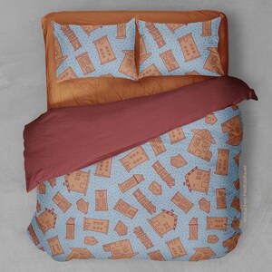 May include: A blue and brown bedding set with a pattern of small houses. The duvet cover and pillowcases feature a repeating pattern of houses on a light blue background. The duvet cover is folded back to reveal a burgundy duvet insert.