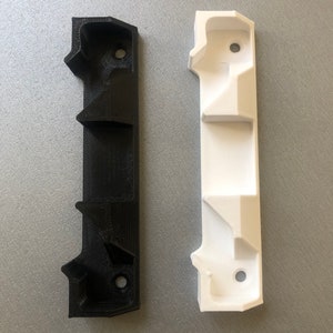 May include: Two 3D printed wall mounts, one black and one white. Each mount has three slots and a hole at the top.