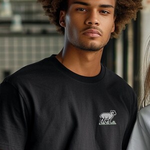 May include: Two people wearing t-shirts with a small embroidered sheep design. The person on the left is wearing a black t-shirt and the person on the right is wearing a white t-shirt.