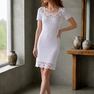 May include: A white crochet dress with a square neckline and short sleeves. The dress features a detailed crochet pattern around the neckline and hem. The model is wearing white high-heeled sandals.