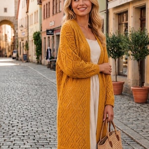 May include: A mustard yellow open-front cardigan featuring an intricate diamond-shaped knit pattern, long sleeves, and ribbed cuffs. The garment is worn over a simple, light beige sleeveless dress, paired with a woven straw handbag with brown accents.