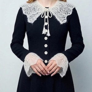 May include: A black dress with a white, lacy collar and cuffs. The dress features a row of white buttons down the front and a tie at the collar. The cuffs and collar have a delicate, openwork design.