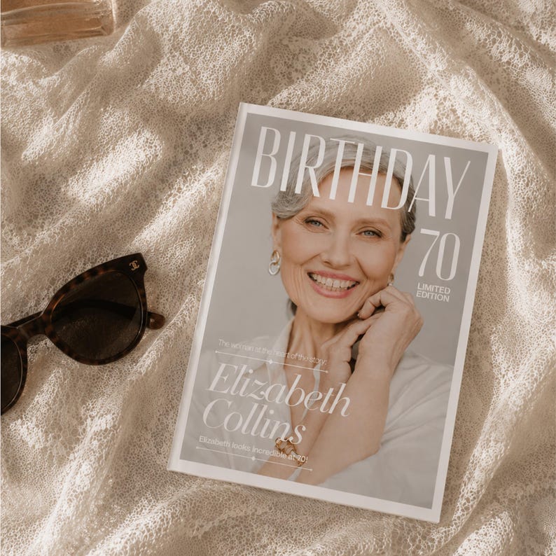 Puede incluir: Una revista titulada "BIRTHDAY 70 LIMITED EDITION" con una mujer sonriente. La portada de la revista incluye el nombre "Elizabeth Collins". Gafas de sol carey descansan sobre una superficie texturizada de color blanquecino.