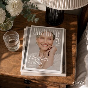 Puede incluir: Una pila de revistas sobre una mesita de noche de madera. La portada de la revista superior dice "BIRTHDAY 70 LIMITED EDITION" con el retrato de una mujer sonriente. La revista tambi&eacute;n presenta el nombre "Elizabeth Collins". Tambi&eacute;n se ven un vaso de agua y una l&aacute;mpara.