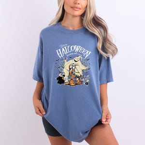 Op de afbeelding: Blauw T-shirt met een afbeelding uit "The Nightmare Before Christmas". Het ontwerp bevat Jack Skellington, Sally, Oogie Boogie en andere personages, met de tekst "Welcome to Halloween".