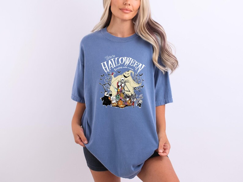 Op de afbeelding: Blauw T-shirt met een afbeelding uit "The Nightmare Before Christmas". Het ontwerp bevat Jack Skellington, Sally, Oogie Boogie en andere personages, met de tekst "Welcome to Halloween".