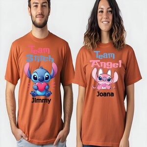 Puede incluir: Dos camisetas color &oacute;xido. Una presenta un personaje de dibujos animados azul sosteniendo un coraz&oacute;n, con el texto "Team Stitch" y "Jimmy". La otra camiseta tiene un personaje rosa, con "Team Angel" y "Joana".