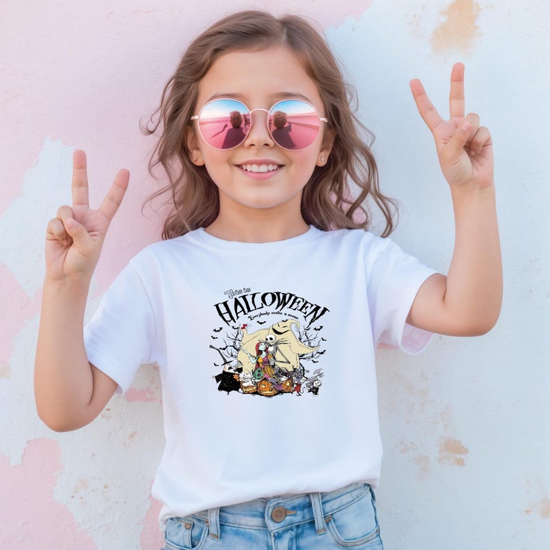 Op de afbeelding: Wit T-shirt met een Halloween-thema grafiek met de tekst "Welcome to Halloween". De afbeelding bevat personages en elementen die bij de feestdag horen. Het shirt wordt door een jong persoon gedragen.