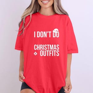 Peut inclure: Un t-shirt rouge avec l'inscription blanche "I DON'T DO CHRISTMAS OUTFITS". Le design comprend un dessin de bonnet de Père Noël au-dessus de "DO" et une décoration de Noël sous "OUTFITS".