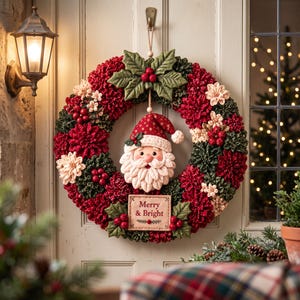 May include: A circular wreath featuring red and dark green fabric petals, cream-colored accents, and holly leaves with red berries. A plush Santa Claus face with a red hat hangs in the center above a rectangular sign that reads Merry & Bright.