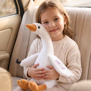 Peut inclure: Une peluche en forme d'oie blanche avec un bec et des pattes orange. Le prénom AMELIA est brodé en fil rose sur l'une des ailes de l'oie. Ce jouet en peluche présente une texture douce et duveteuse ainsi qu'un long cou.