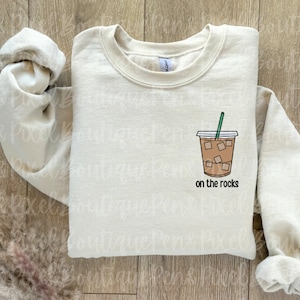 May include: A beige sweatshirt with a graphic of a cup of iced coffee and the text "on the rocks".
