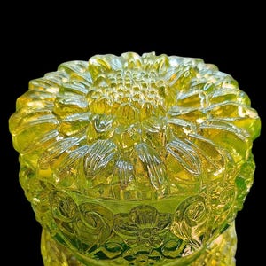 Peut inclure: Un bol décoratif en verre jaune-vert avec un motif de tournesol. Le bol présente un motif floral détaillé et est posé sur un fond noir. Le verre a une surface texturée et réfléchissante.