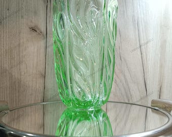 May include: A green glass vase with a swirling, textured design. The vase is sitting on a silver, round, mirrored surface.
