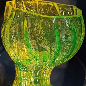 Op de afbeelding: Een felgroene en gele glazen vaas met een unieke, getextureerde, organische vorm. De vaas heeft een brede, open bovenkant en een smalle basis.