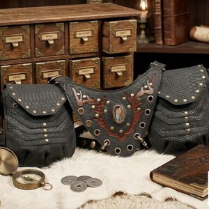 Boho leather shoulder harness with two reptile-texture pouches and brass hardware, photographed overhead on fur with travel compass, leather notebooks, old coins, and bottle.