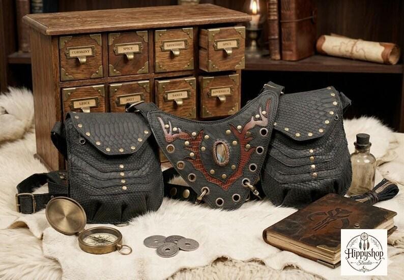 Boho leather shoulder harness with two reptile-texture pouches and brass hardware, photographed overhead on fur with travel compass, leather notebooks, old coins, and bottle.