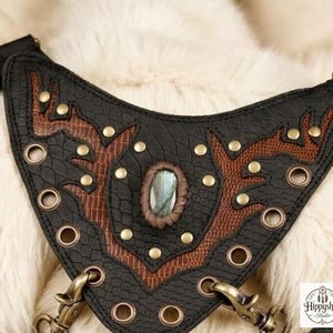Steampunk inspired leather harness purse set with double front pockets and brass accents, styled on cream fur alongside antique compass, embossed leather notebooks, and glass bottle.