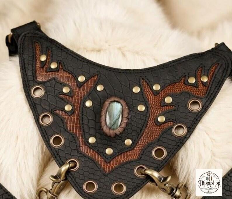 Steampunk inspired leather harness purse set with double front pockets and brass accents, styled on cream fur alongside antique compass, embossed leather notebooks, and glass bottle.