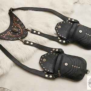 Alternative fashion leather chest bag with symmetrical studded pouches and textured finish, flat lay display with vintage compass, brown leather journals, coins, and flask.