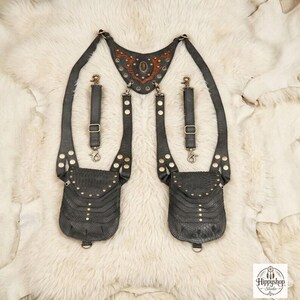 Handcrafted black leather body harness with reptile embossed pouches and metal hardware, styled overhead with antique compass, embossed notebooks, and decorative coins.