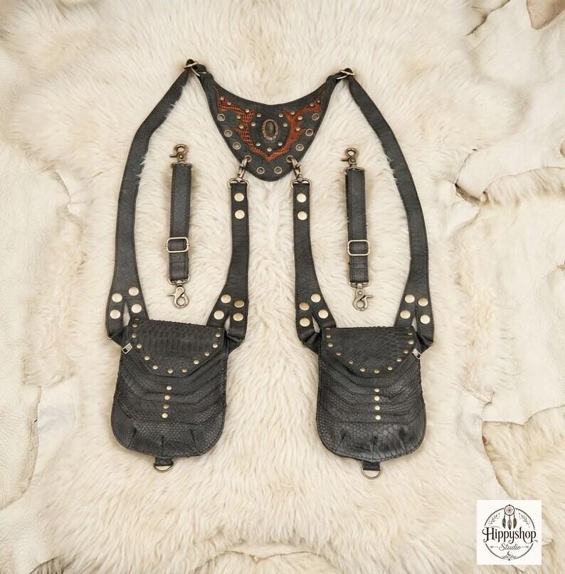 Handcrafted black leather body harness with reptile embossed pouches and metal hardware, styled overhead with antique compass, embossed notebooks, and decorative coins.