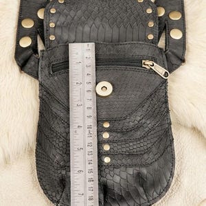 Dual pouch leather chest harness with brass studs and textured flap pockets, laid flat with explorer accessories including compass, leather journals, old coins, and flask.