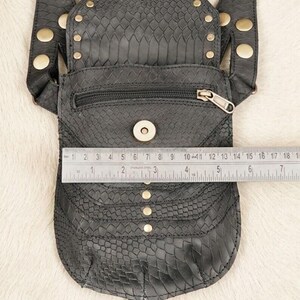 May include: A black textured bag with a snake-skin pattern, brass-colored studs, and a magnetic snap closure. A metal ruler placed across the center shows a width of approximately 6.5 inches. The bag features a zippered pocket and a bottom D-ring.