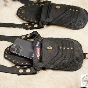 Bohemian leather body harness purse with reptile pattern pouches and brass hardware, flat lay photography on fur with antique compass and rustic travel props.