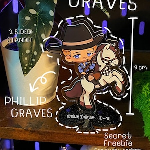 May include: A 8 cm tall, two-sided standee featuring a cartoon cowboy on a horse. The standee has a black base with the text "SHADOW 0-1". The text "COWBOY GRAVES" and "PHILLIP GRAVES" are also visible.