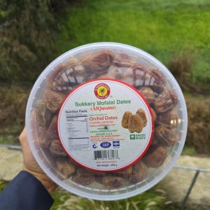 Puede incluir: Un recipiente de plástico transparente lleno de dátiles Sukkary Mofatal (AlQassim). El recipiente tiene una etiqueta roja y blanca con el texto "Orchid Dates" y "Saudi Made". El peso neto es de 800 g.