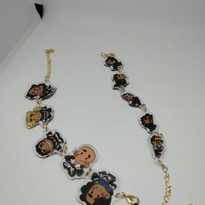 Pode incluir: Um bracelete de corrente dourada com pingentes de acrílico transparente com personagens de desenhos animados. Os pingentes são de pessoas diferentes com vários penteados e roupas.