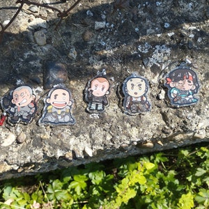 Pode incluir: Seis chaveiros de personagens de desenhos animados coloridos com diferentes expressões. Os chaveiros são feitos de plástico transparente e apresentam uma variedade de personagens, incluindo um soldado, um piloto e um robô. Os chaveiros são exibidos em uma superfície de concreto cinza.