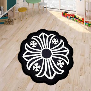 May include: A round, black and white rug with a floral design. The rug features a central black circle surrounded by white petal-like shapes and four-point star accents. The rug is placed on a light wood floor.