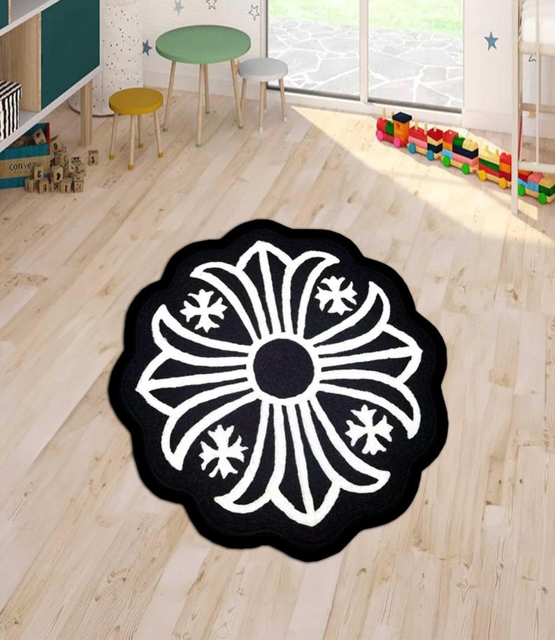 May include: A round, black and white rug with a floral design. The rug features a central black circle surrounded by white petal-like shapes and four-point star accents. The rug is placed on a light wood floor.