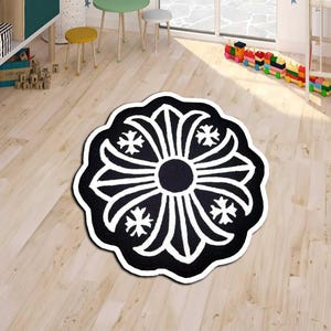 May include: A black and white floral-patterned rug with a circular design. The rug features a central black circle surrounded by white, petal-like shapes and starburst accents. The rug is placed on a light-colored wooden floor.