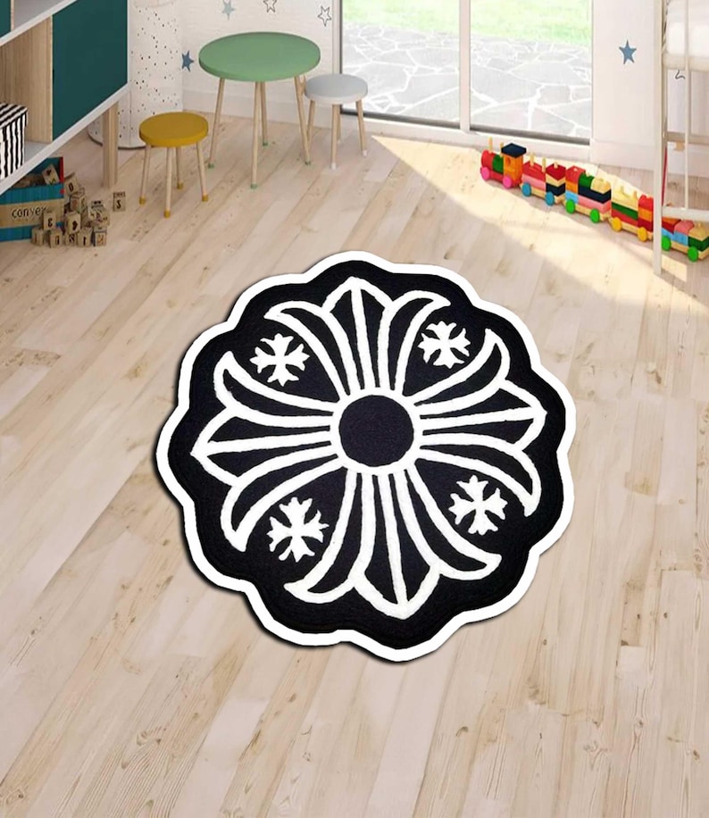 May include: A black and white floral-patterned rug with a circular design. The rug features a central black circle surrounded by white, petal-like shapes and starburst accents. The rug is placed on a light-colored wooden floor.