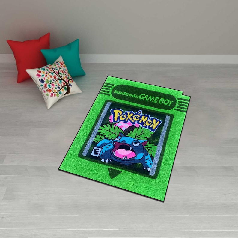 May include: A green rectangular rug featuring a design inspired by a Nintendo Game Boy Pokemon cartridge. The rug displays the Pokemon logo and a blue and pink cartoon character. The text "Nintendo GAME BOY" is at the top.