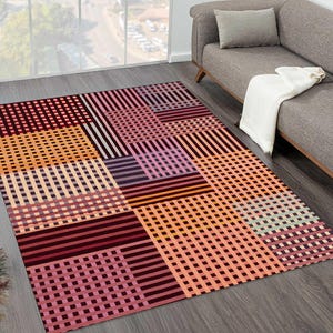 May include: A rectangular area rug with a geometric pattern. The rug features a patchwork design with squares and rectangles in shades of orange, pink, burgundy, and purple. The pattern includes both solid stripes and a grid-like design.