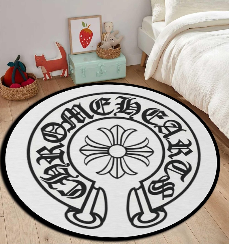 May include: Round white rug with a black border featuring a black gothic-style emblem. The emblem includes a floral design at the center, surrounded by text in a gothic font. The rug is placed on a wooden floor.
