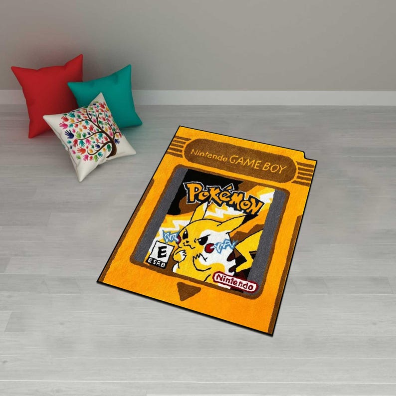May include: A rectangular rug designed to resemble a Nintendo Game Boy cartridge. The rug features the Pok&eacute;mon logo and a yellow Pikachu character. The rug is yellow with black and gray accents and the text "Nintendo GAME BOY".