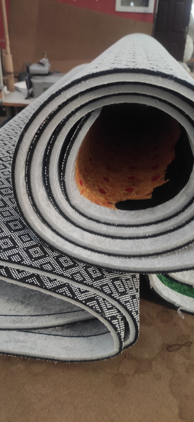 Peut inclure: Un tapis enroul&eacute; avec un motif g&eacute;om&eacute;trique noir et blanc. Le tapis a un dos blanc et est enroul&eacute; serr&eacute;. Le tapis est sur une surface brune.