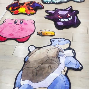 May include: A collection of character-shaped rugs, including a pink Kirby, a yellow Lightning McQueen car, and various Pok&eacute;mon like Charizard, Blastoise, and Gengar. The rugs are colorful and designed with detailed outlines.