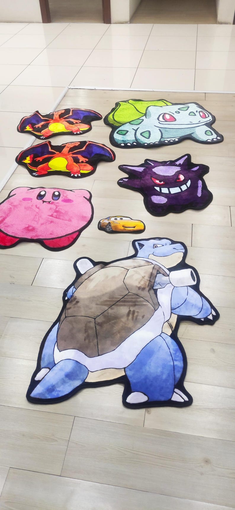 May include: A collection of character-shaped rugs, including a pink Kirby, a yellow Lightning McQueen car, and various Pok&eacute;mon like Charizard, Blastoise, and Gengar. The rugs are colorful and designed with detailed outlines.