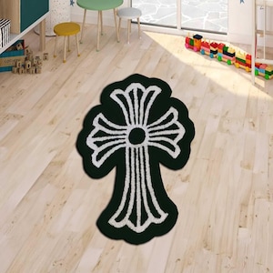 May include: A dark green rug with a white cross design. The rug is placed on a light wood floor. The cross design has a circular center and stylized arms. The rug is a decorative floor covering.